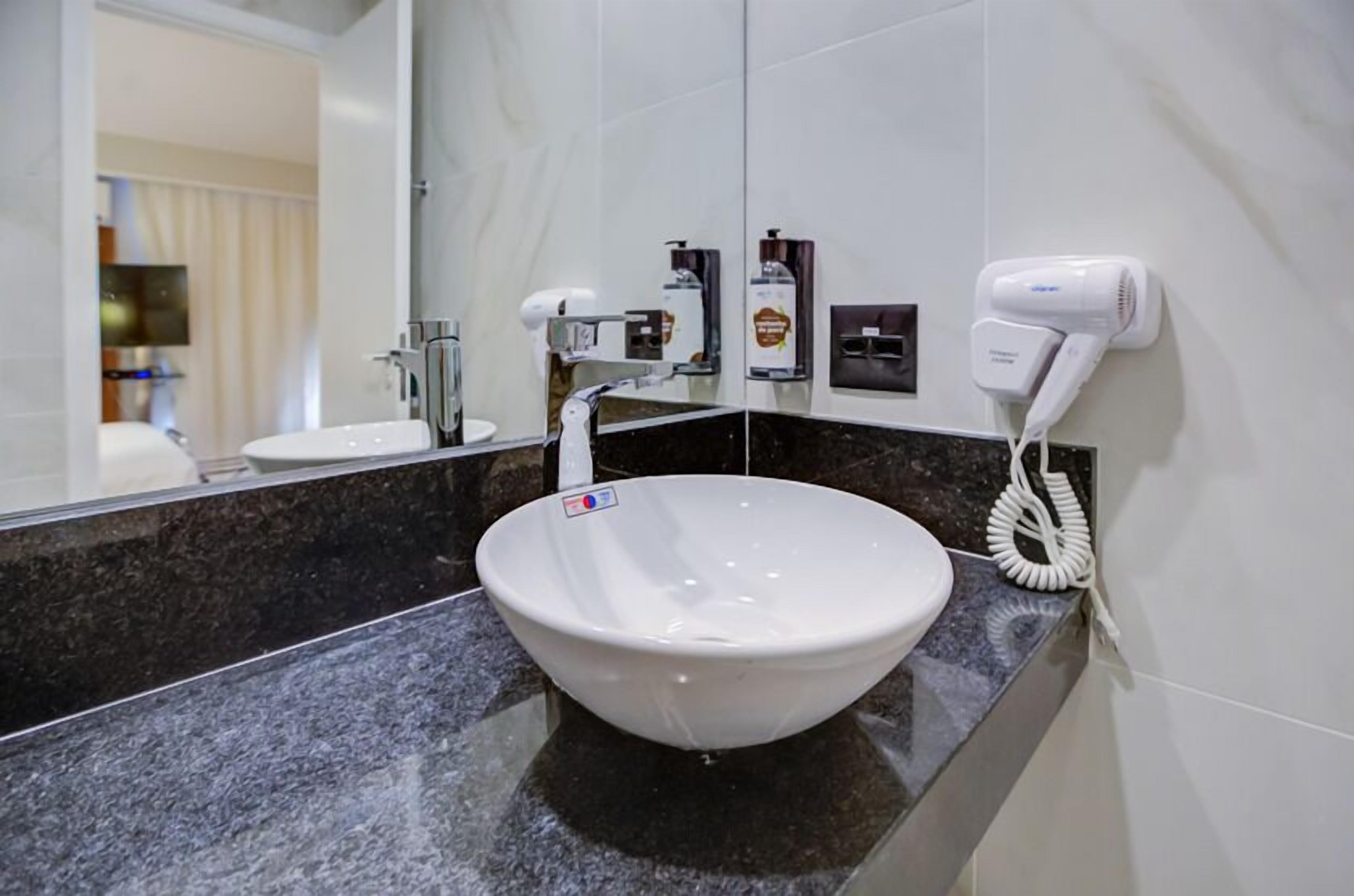 Baño con lavamanos blanco, secador de pelo y artículos de tocador en la pared.