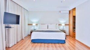 Een hotelkamer met een bed, gordijnen, een flatscreen televisie, bedlampen en een airconditioning.