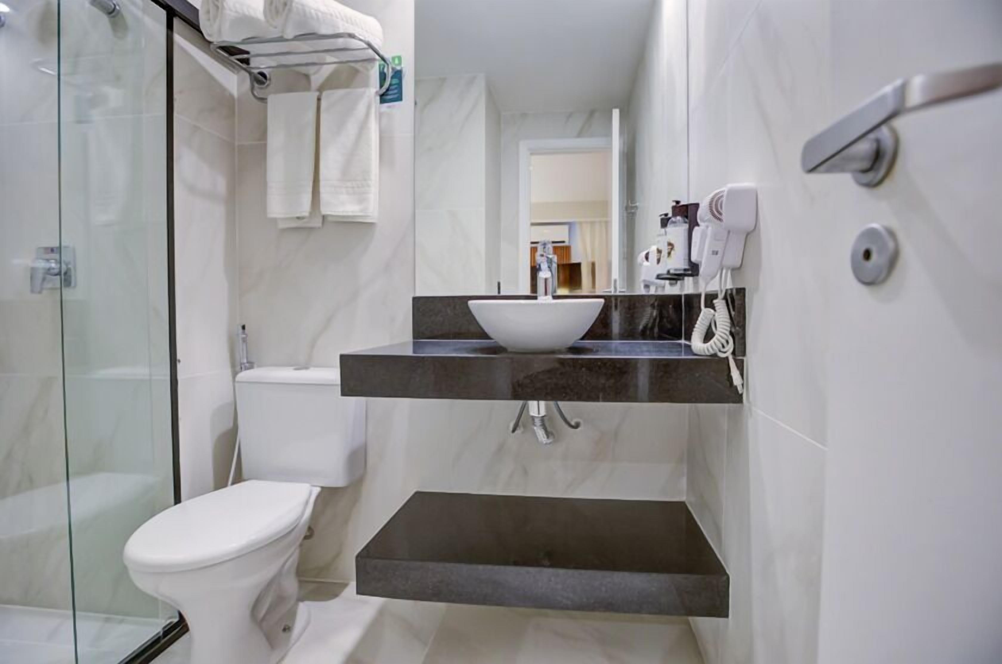 A bathroom with a glass shower enclosure, a white toilet, a sink with a marble countertop, and a towel rack.