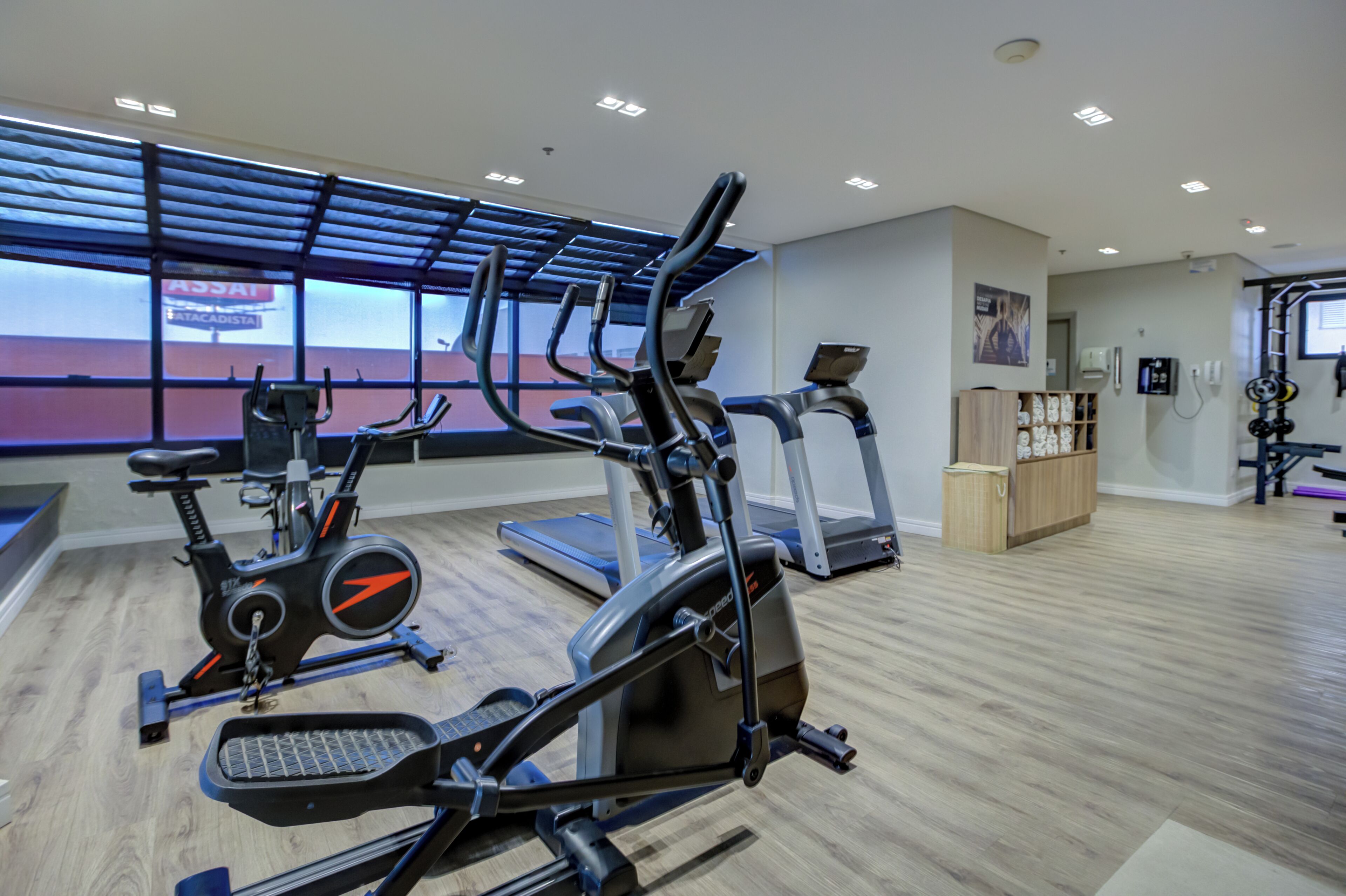 Un gimnasio con diverso equipo de ejercicio, incluyendo bicicletas estáticas y cintas de correr, y un amplio ventanal que proporciona luz natural.