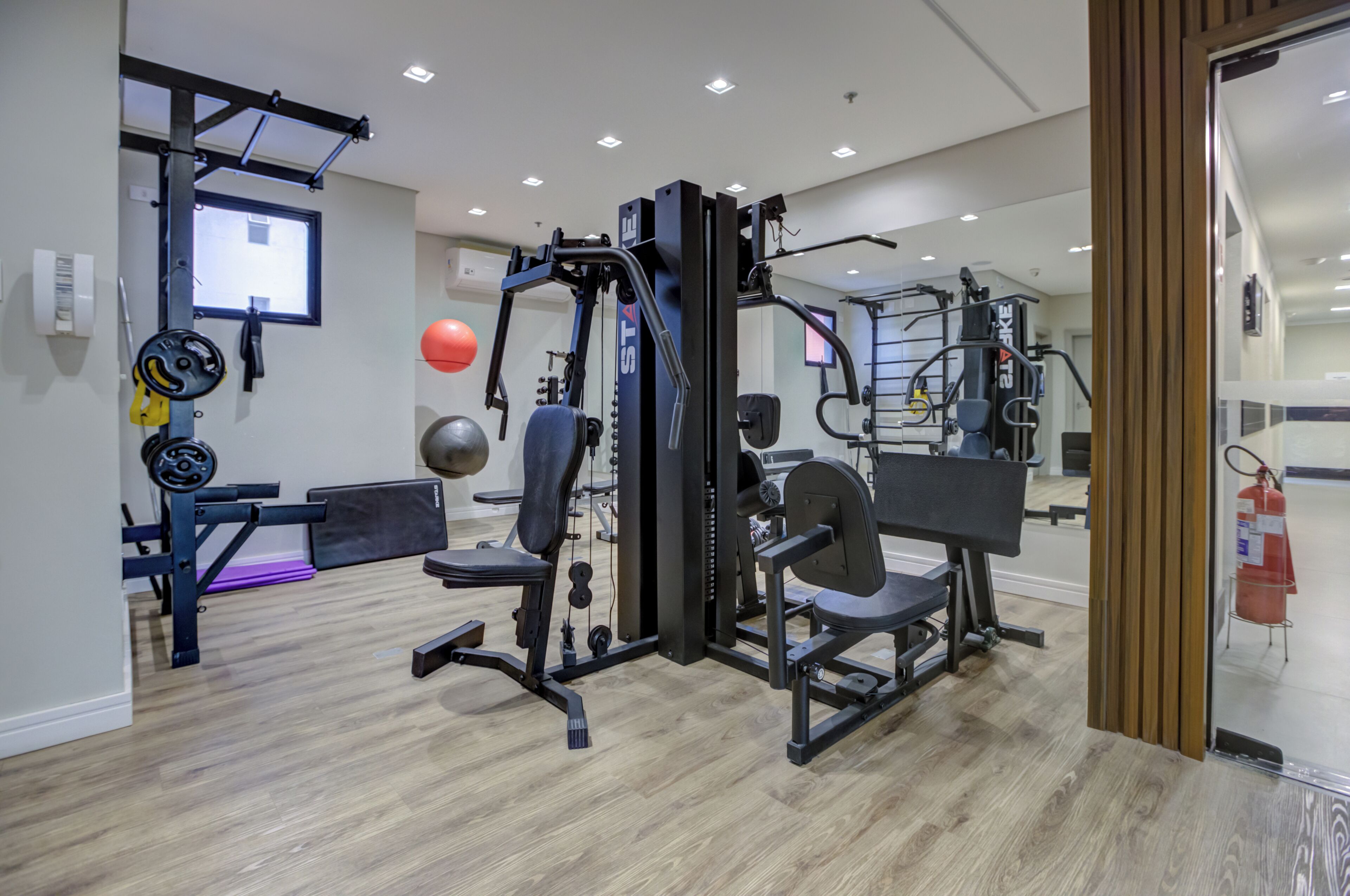 Un gimnasio con diversos equipos de ejercicio, un espejo y un extintor.