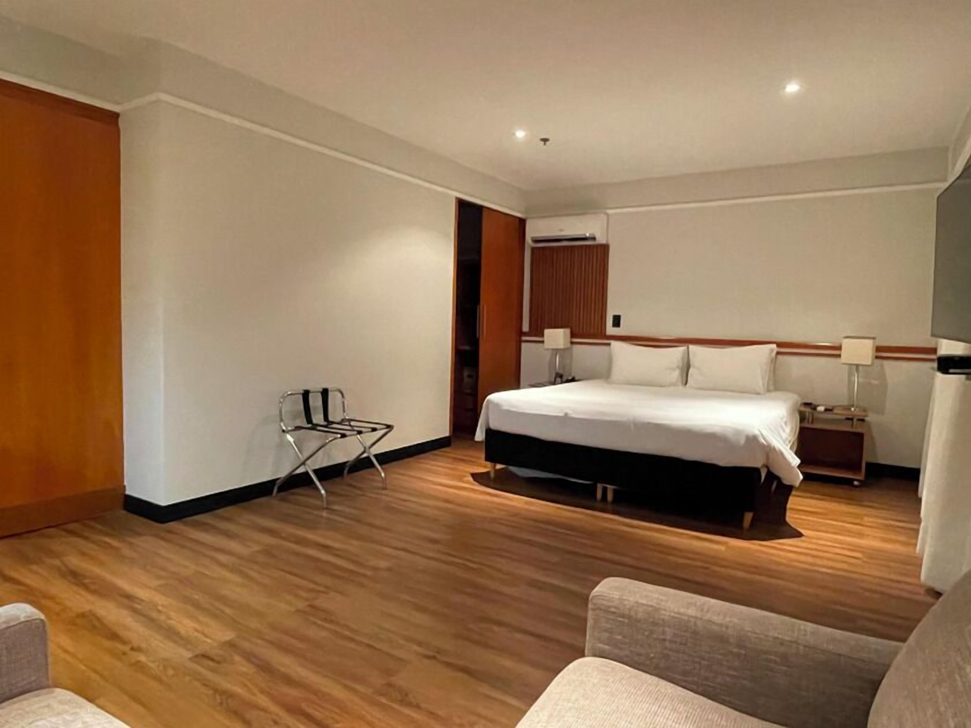 Habitación de hotel con una cama grande, mesitas de noche, una silla y suelo de madera.