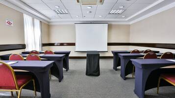 Un salón de conferencias con mesas y sillas, una pantalla de proyector y suelo alfombrado.