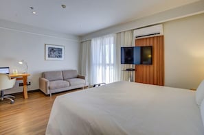 Habitación de hotel con una cama grande, un sofá, un escritorio con computadora y un televisor.