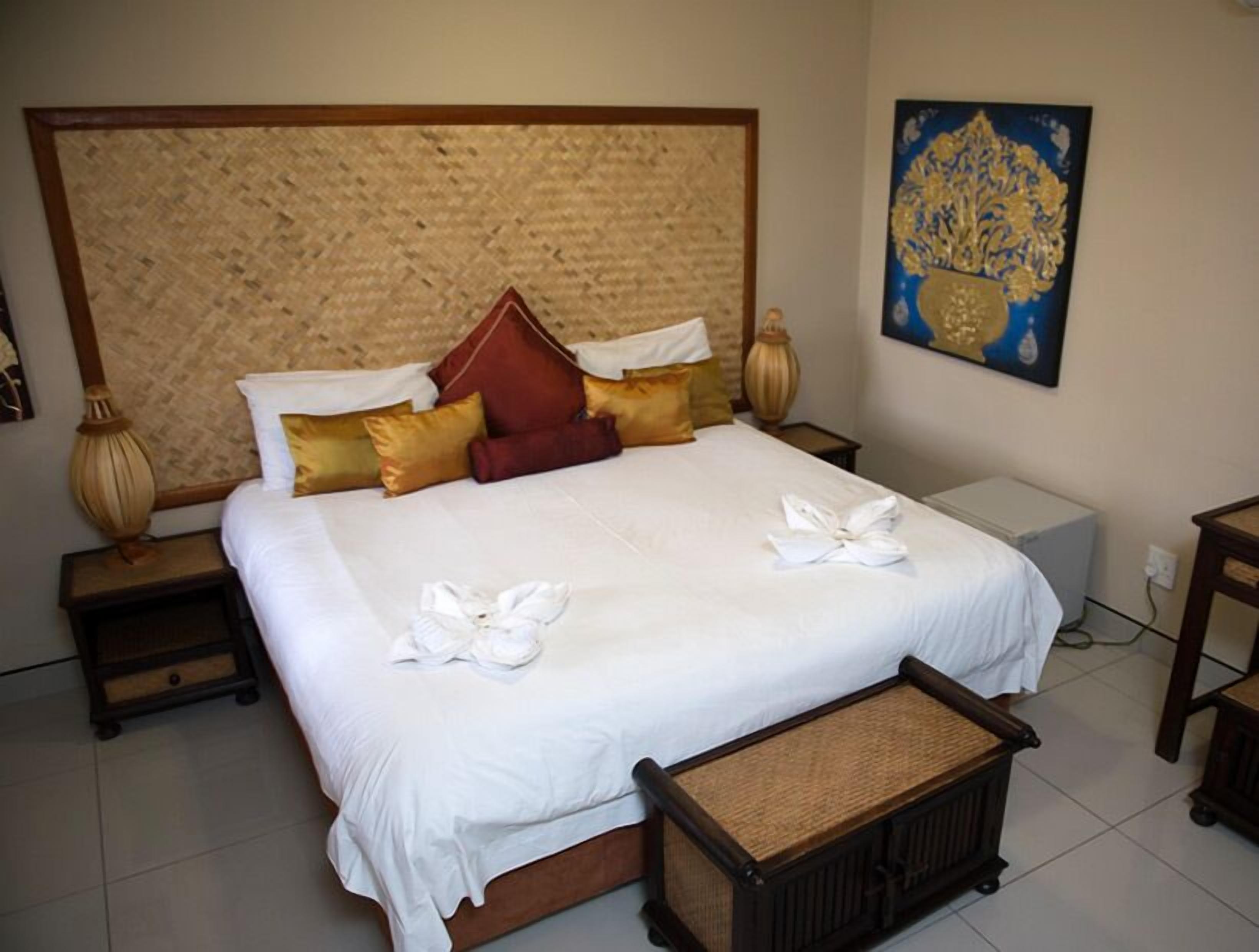 A neatly made bed with white linens and decorative pillows, a woven headboard, and a small bedside table with a lamp.
