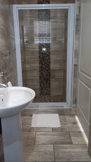 A shower with a glass door, a white sink, and a small rug on the floor. - Midrand Conference Centre (Midrand)