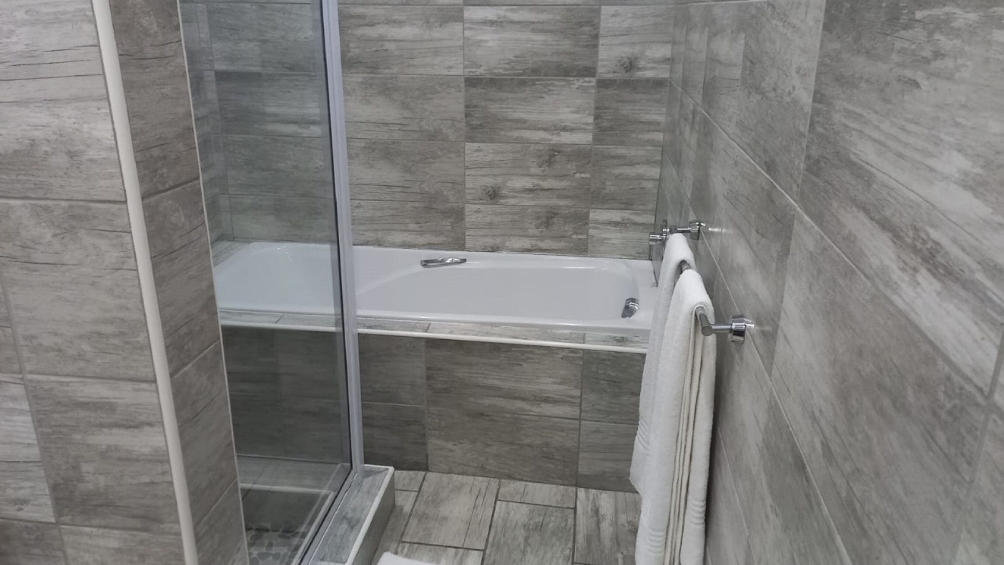 A modern shower area with a glass door, a bathtub, and a towel rack.