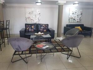 A living room with two sofas, a coffee table, and two armchairs. There are floral paintings on the walls and a pillar in the center. - Midrand Conference Centre (Midrand)