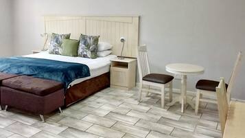 Un dormitorio con una cama, una mesita de noche, una silla, una pequeña mesa y un banco.