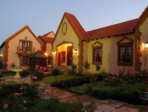 A traditional house with a red-tiled roof, stone pillars, and a well-maintained garden with pink flowers. - Midrand Conference Centre (Midrand)