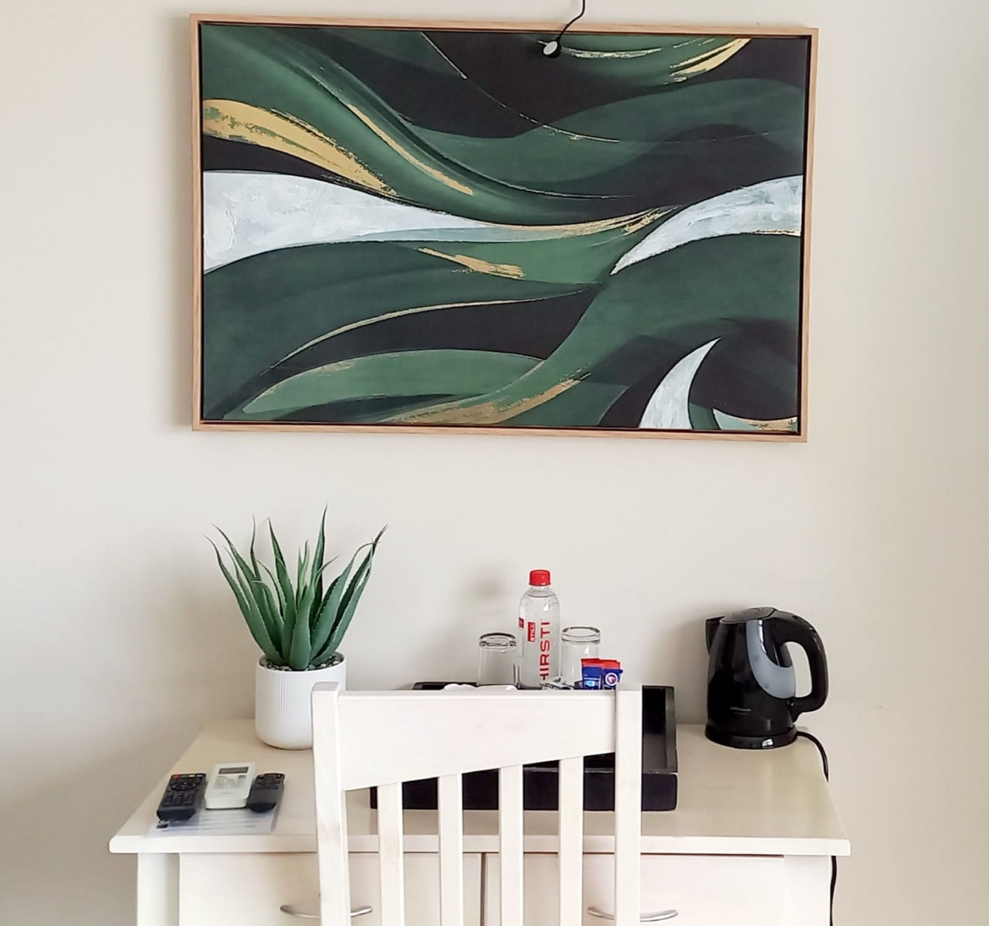 A white desk with a potted plant, a water bottle, a coffee maker, and a remote control.