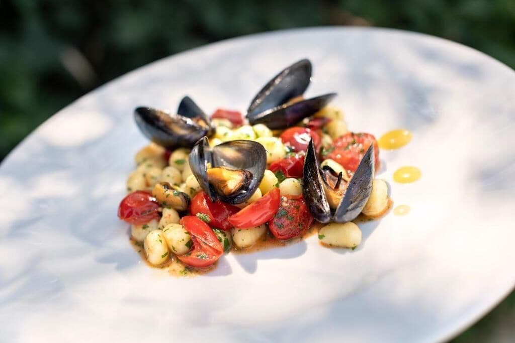 Un plato de mejillones con tomates y hierbas.