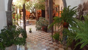 An indoor courtyard with a tiled floor, potted plants, and a large archway. - Suites Santo Domingo (San Miguel de Allende)