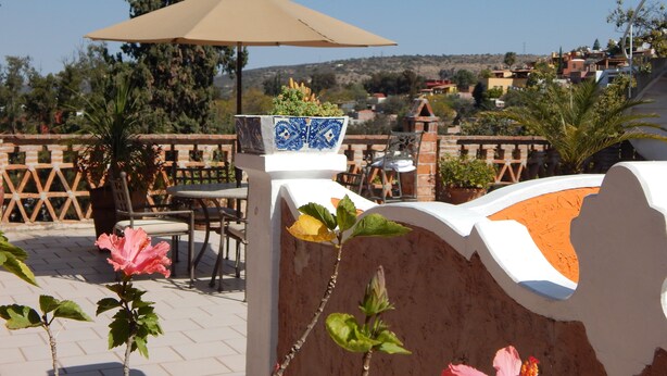 A patio area with a table and chairs, a decorative planter, and a view of a hillside town. - Suites Santo Domingo (San Miguel de Allende)