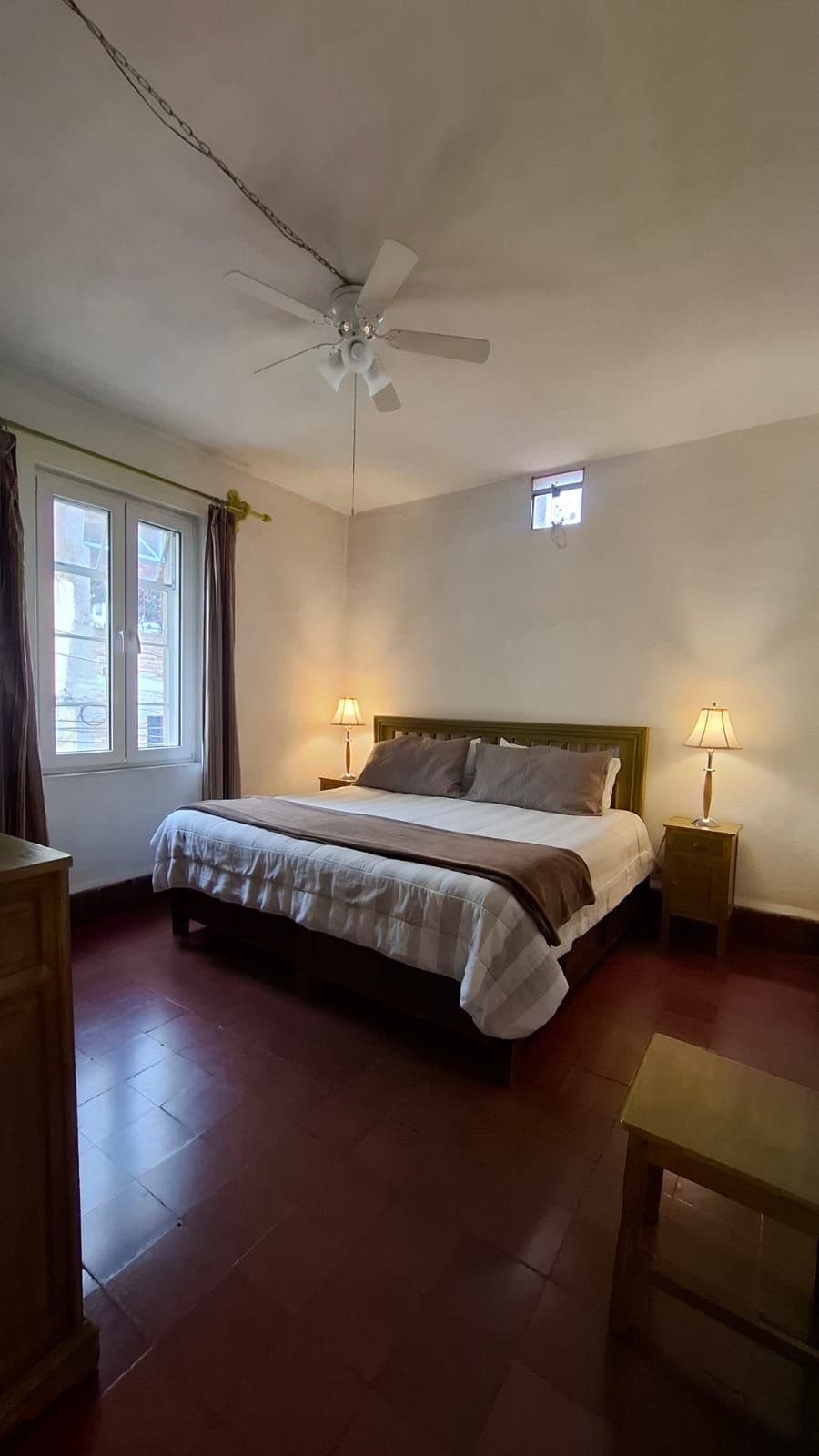 A bedroom with a bed, bedside lamps, a ceiling fan, and a window with curtains.