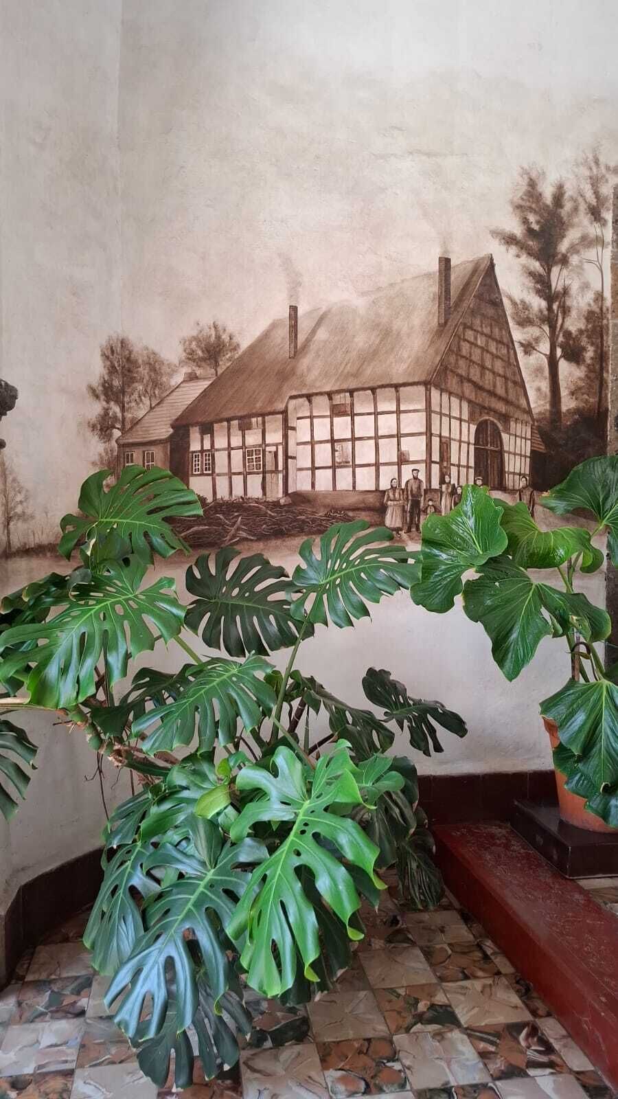 Ein Wandgemälde eines Hauses im traditionellen Stil mit einem Strohdach, einem Schornstein und einer Gruppe von Personen davor.