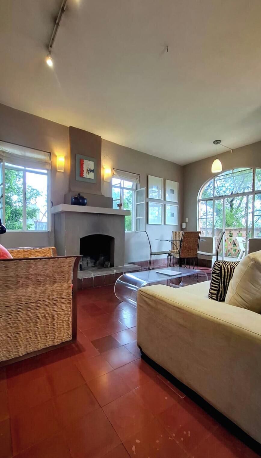 Una sala de estar con chimenea, un sofá, un sillón de mimbre y una mesa de comedor.