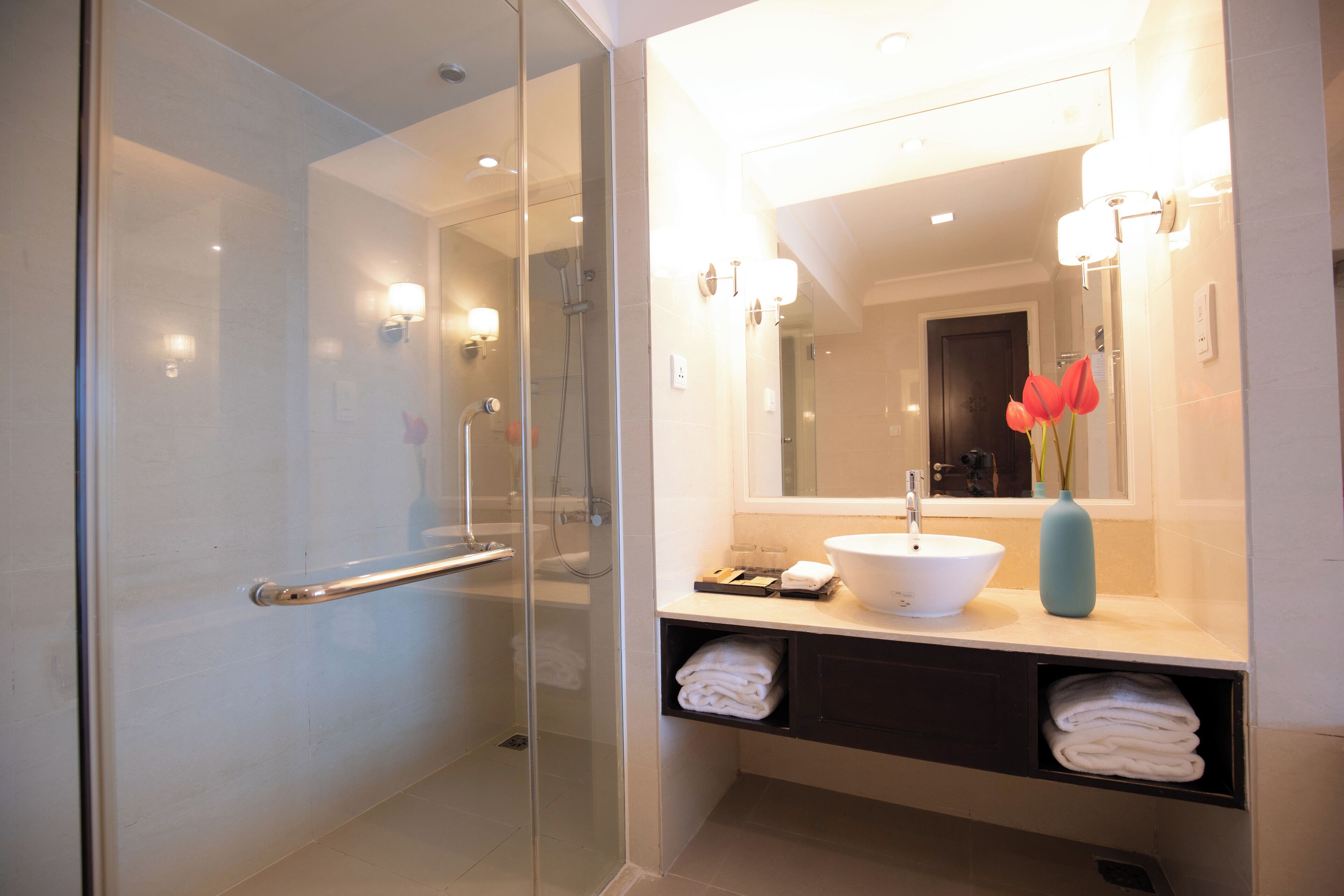 A modern bathroom with a glass-enclosed shower, a white sink, and a mirror with lights.