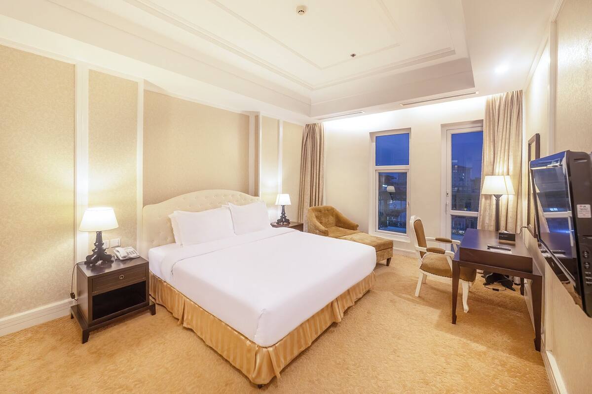 A hotel room with a large bed, a desk, a chair, and a TV.