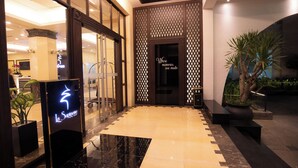 Entrada de hotel com design moderno, apresentando um piso de azulejos preto e bege, uma parede decorativa com padrão geométrico e uma placa com o nome 'La Sapineva'.