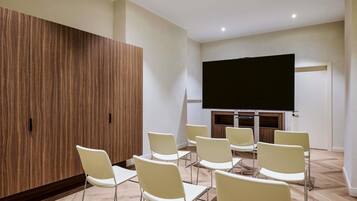 Un salón de conferencias con una gran pantalla plana, sillas blancas y un panel de pared de madera.