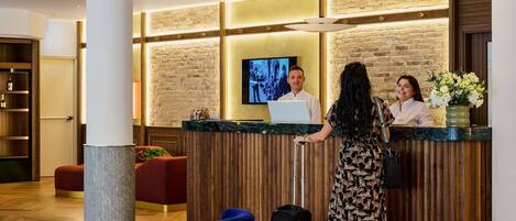 A hotel reception area with a wooden reception desk, a television, and a modern interior design.