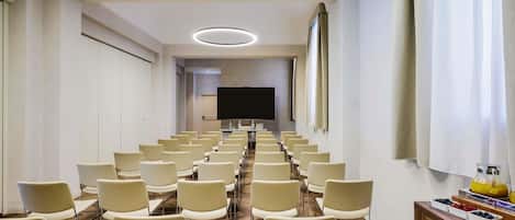A conference room with rows of chairs, a large screen, and a buffet table with fruits and pastries.