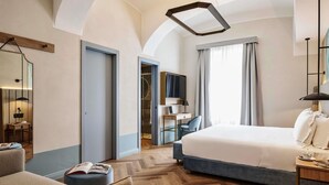 A modern hotel room with a large bed, a desk with a laptop, a chair, and a small seating area with a book. - Hotel Giacomo Morra Alba - Handwritten Collection (Alba)