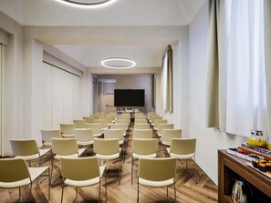 Un salón de conferencias con filas de sillas, una pantalla grande y una mesa de buffet con comida.