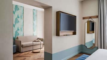 Una habitación de hotel con sofá, televisión, espejo y piso de madera.