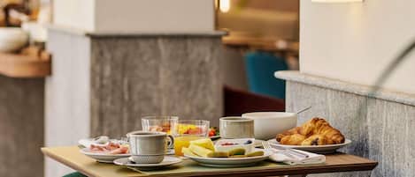 Una mesa de desayuno con platos de comida, tazas y un croissant.