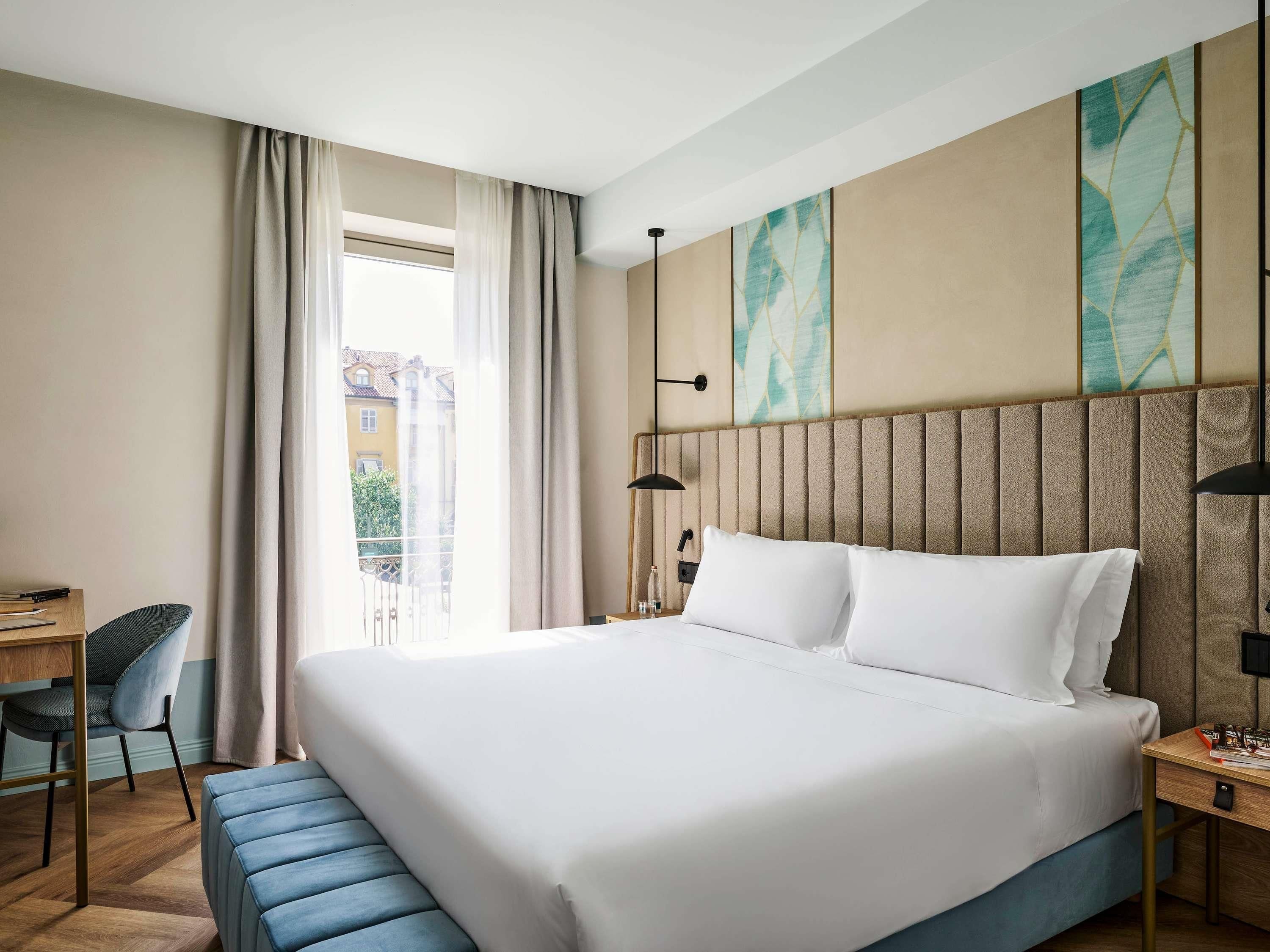 A hotel room with a large bed, a desk, a chair, and a view of the outside.