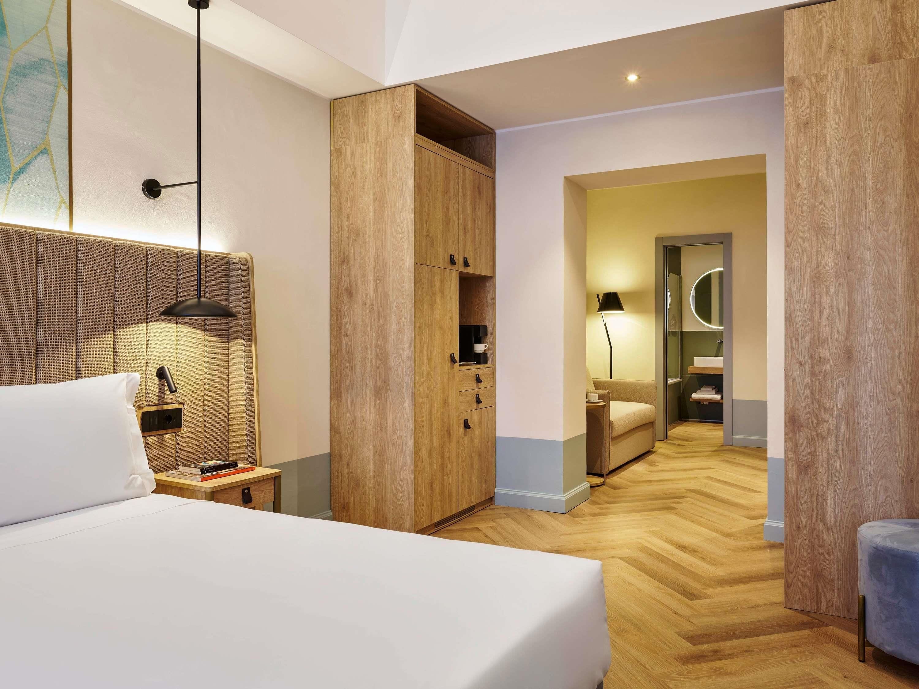 Een hotelkamer met een bed, nachtkastje, lamp, garderobe en uitzicht op de badkamer.