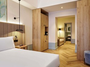 Ett hotellrum med en säng, ett nattduksbord, en lampa, en garderob och utsikt in i badrummet.