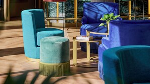 A modern lounge area with teal and blue upholstered seating, a small round table, and a potted plant.