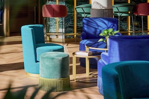 Een moderne zithoek met teal- en blauwe bekleding, een klein rond tafeltje en een potplant.