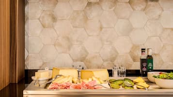 Buffet com queijo, carnes e frutas, e duas garrafas de azeite sobre um balcão com azulejos hexagonais.