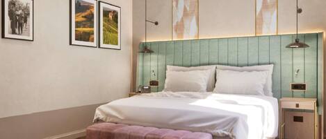 A modern bedroom with a large bed, a bench, and two bedside tables. There are framed pictures on the wall.
