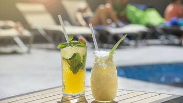 Two drinks on a table by a poolside with lounge chairs in the background.