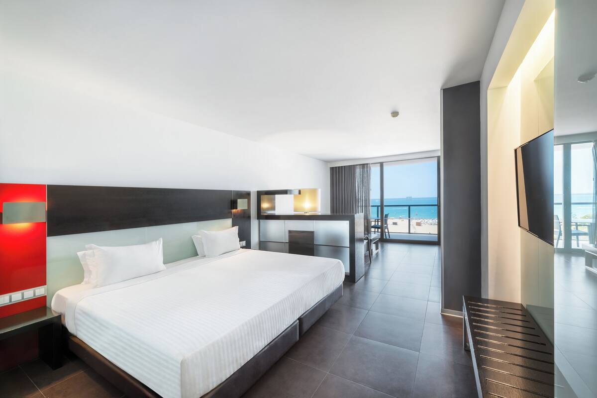 A modern hotel room with a large bed, a desk, and a balcony with a view.
