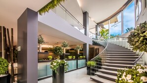 A modern hotel lobby with a staircase, indoor plants, and a view of the sky through large windows. - RR Hotel da Rocha (Portimão)