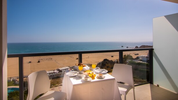 A balcony with a table set for breakfast overlooking a beach and the ocean. - RR Hotel da Rocha (Portimão)