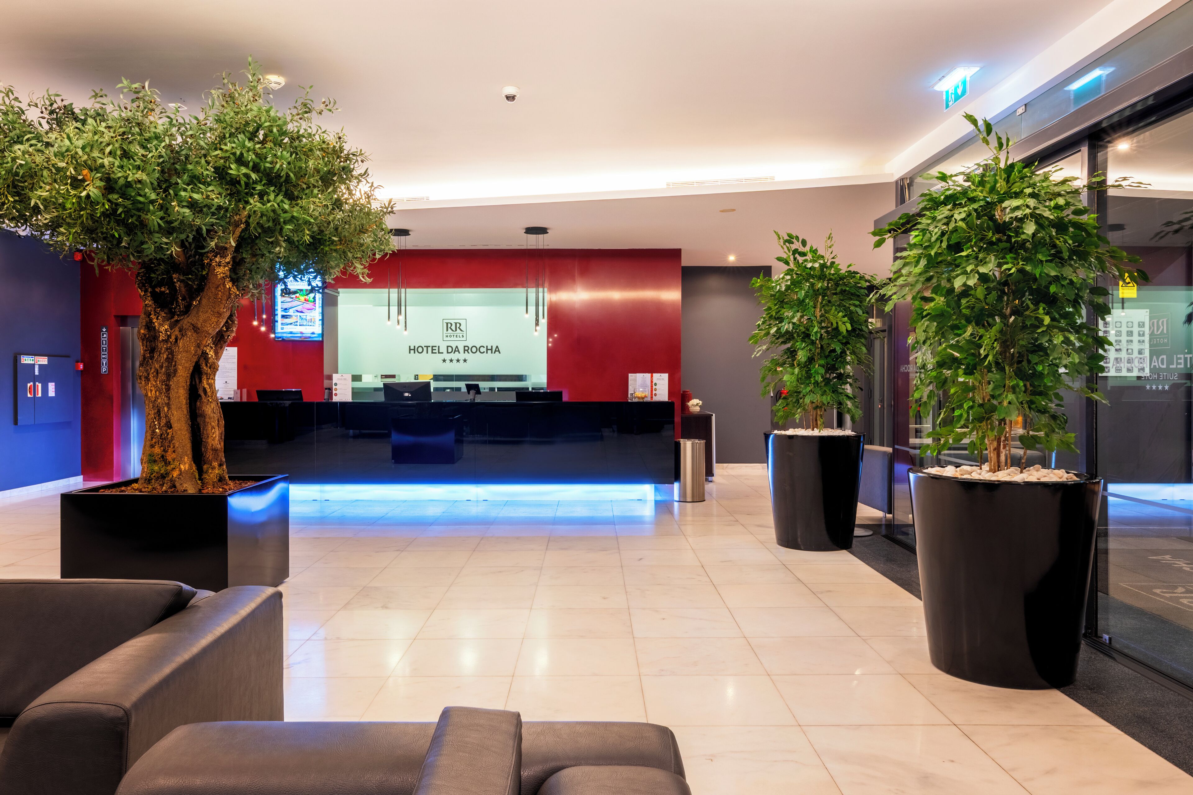 A hotel reception area with a modern design, featuring a reception desk, seating area, and potted plants.