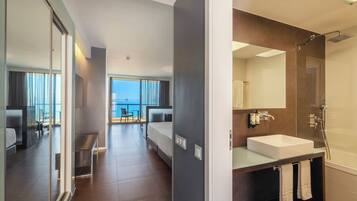 A modern hotel room with a balcony, a large bathroom with a glass shower, and a view of the sea.