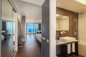 A modern hotel room with a balcony, a large bathroom with a glass shower, and a view of the sea.