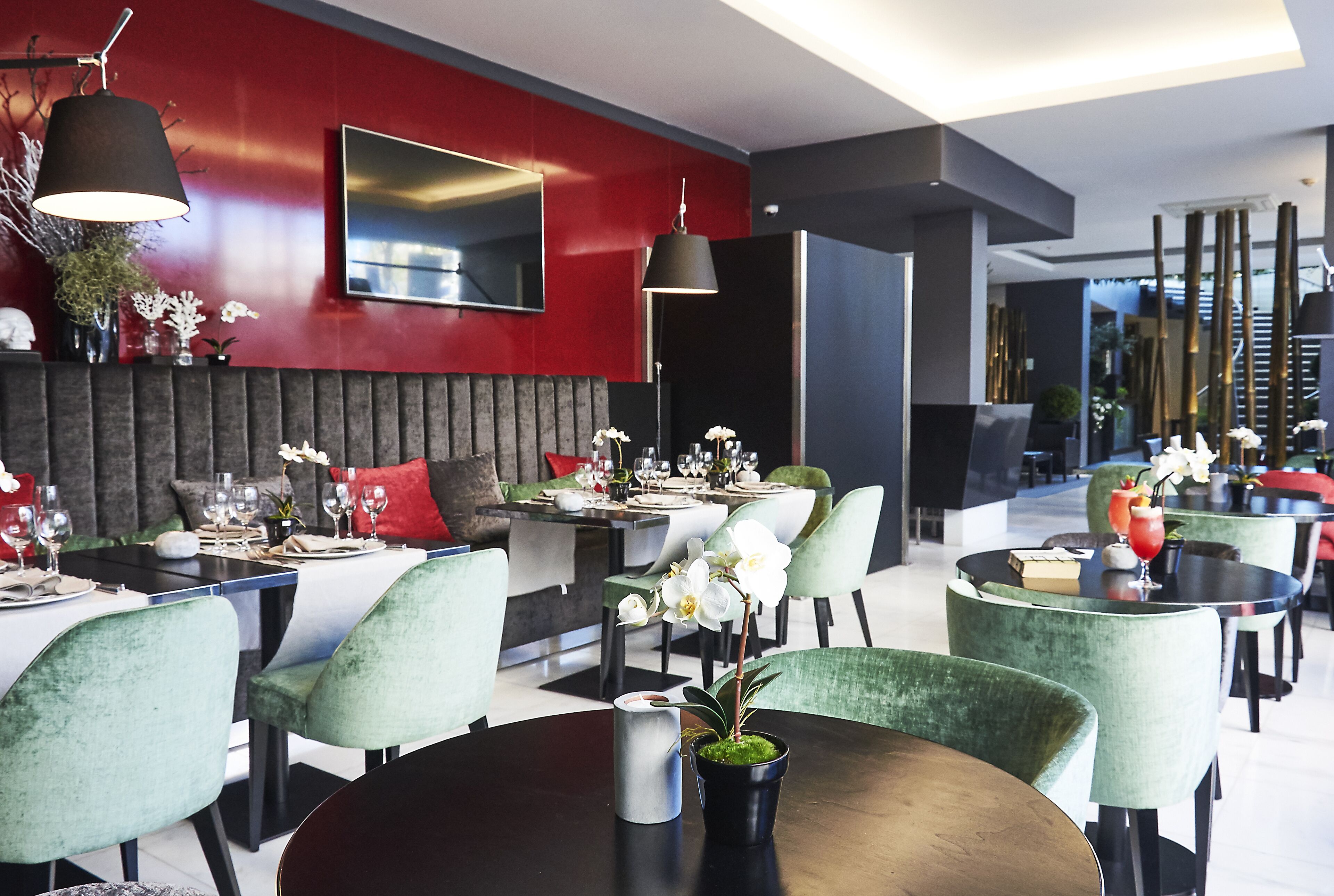 Un restaurant modern amb taules rodones, cadires de vellut verd i parets vermelles.
