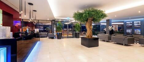 A modern lobby with a reception desk, seating area, and a large tree planter.