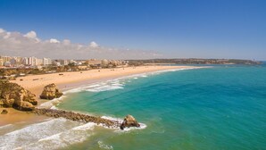 A coastal cityscape with a wide sandy beach, rocky outcrops, and a clear blue sea. - RR Hotel da Rocha (Portimão)