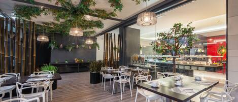 Un restaurante moderno con sillas y mesas blancas, plantas colgantes y vistas al área de la cocina.