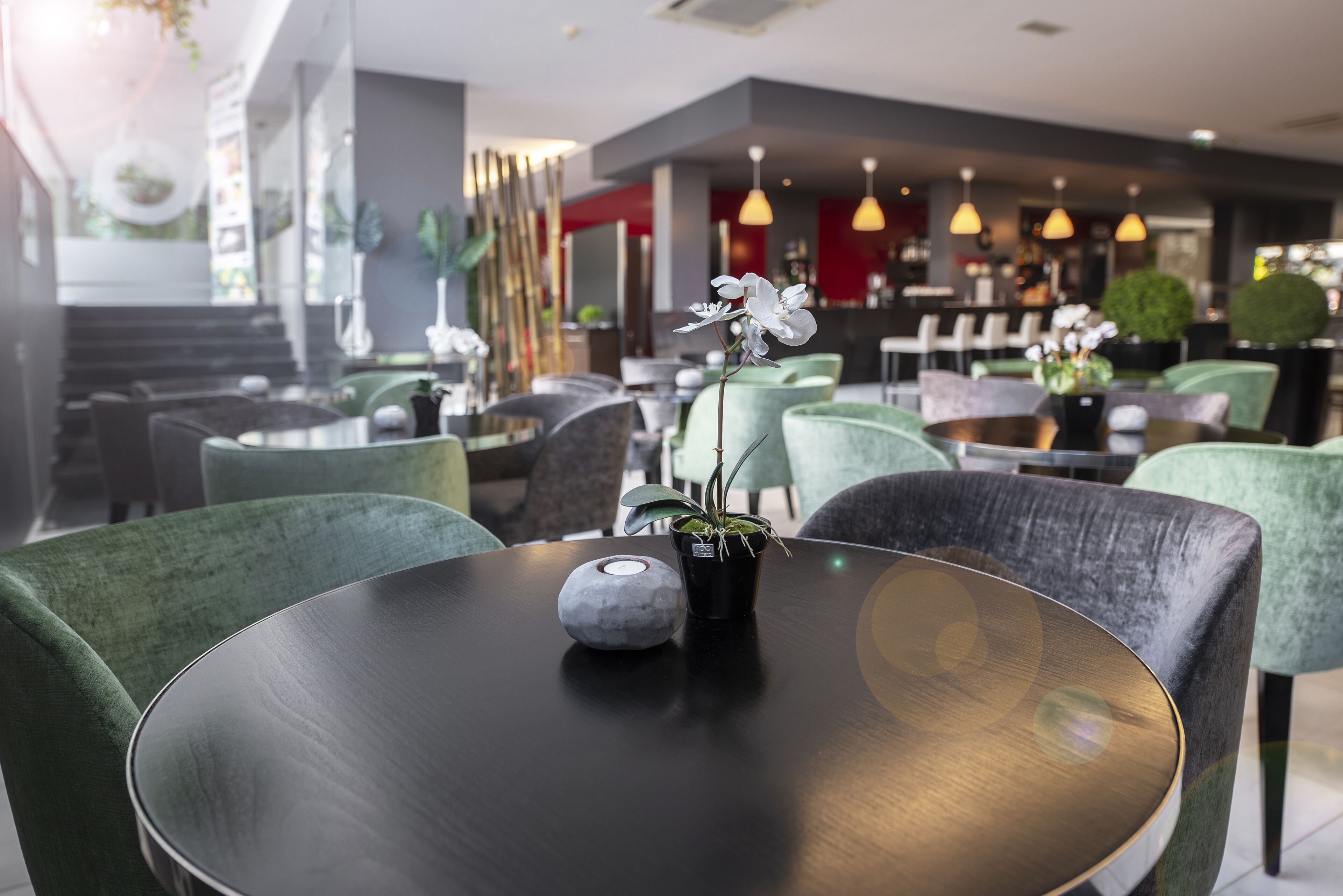 A modern dining area with round tables, green upholstered chairs, and a potted orchid on one table.